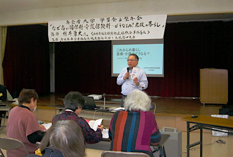 「社会保障は国の責任で」と講演する札幌社保協の村井事務局長と熱心に話を聞く組合員