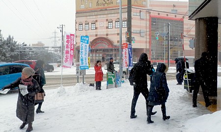 降りしきる雪のなか、通勤通学客らに呼びかける吉岡さんと後援会員