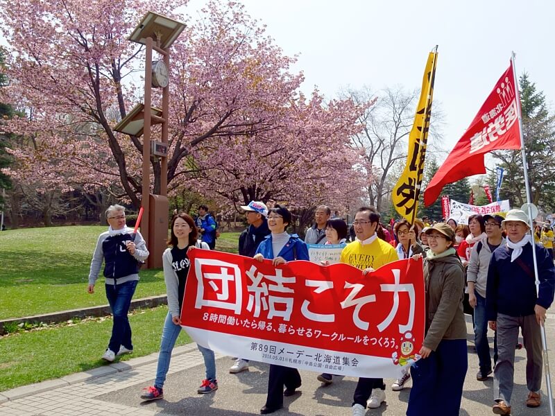 紙議員、黒澤実行委員長らを先頭に満開の桜のもとをメーデー行進する人たち